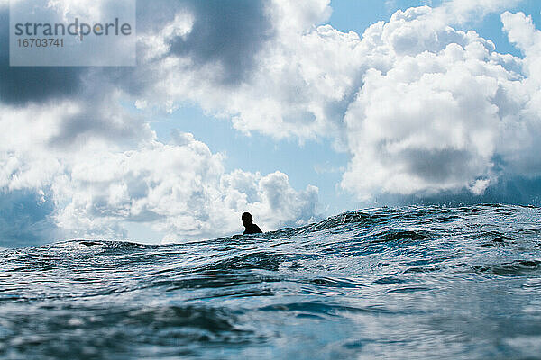 Surfer sitzt allein unter einem stimmungsvollen Himmel im Meer