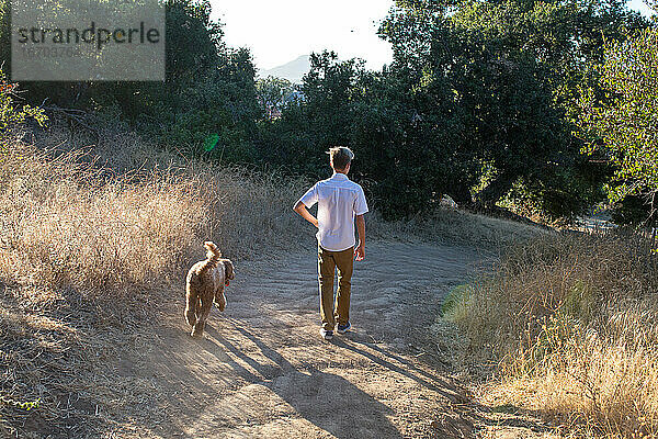 Der Rücken eines Jungen und seines Hundes auf einem Wanderweg
