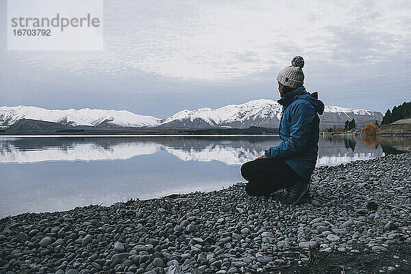 Junge Frau kniet am Lake Tekapo nieder und blickt auf die Südalpen