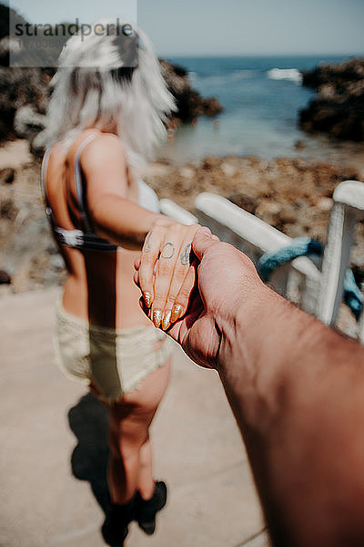 Ein Paar geht am Strand Hand in Hand spazieren. Perspektive vom Arm des Mannes aus