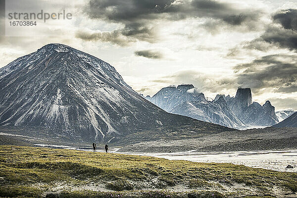 Silhouette von zwei Rucksacktouristen  die über einen dramatischen Bergpass wandern.