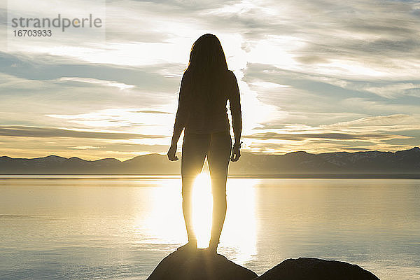 Rückansicht der Silhouette einer Frau auf einem Felsen am Lake Tahoe bei Sonnenuntergang