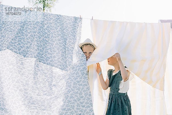 Bruder und Schwester spielen in der Wäsche  die im Sommer auf der Leine trocknet