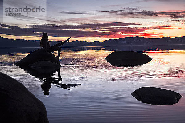 Silhouette Frau sitzt auf einem Felsen inmitten des Lake Tahoe gegen den Himmel bei Sonnenuntergang