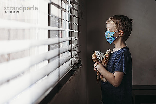 Seitenansicht eines Jungen im Schulalter mit Maske und Stofftier