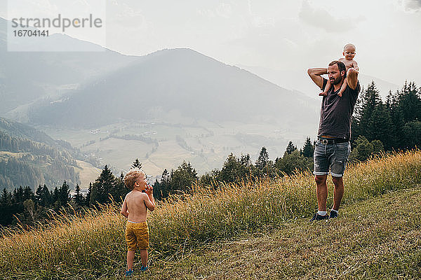 Vater mit Baby auf den Schultern schaut auf junges männliches Kleinkind in den Bergen