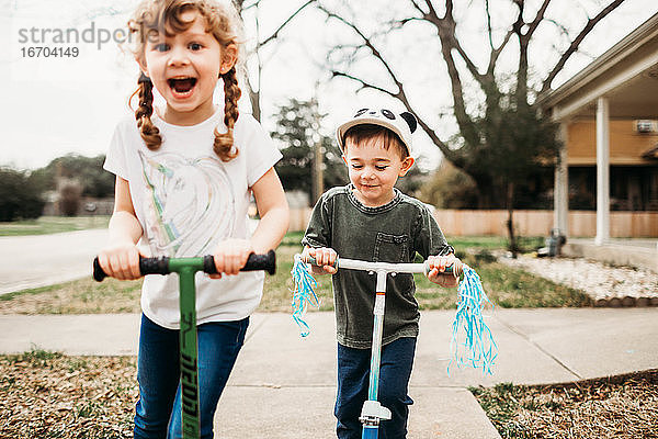Junge Schwester und Bruder fahren Roller draußen im Vorgarten