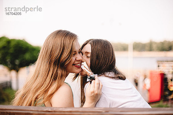 Glückliches lesbisches Paar  das auf einer Bank sitzend Eiscreme isst