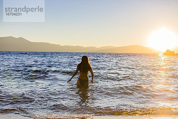 Teenagerschwimmen im Bergsee bei Sonnenuntergang oder Sonnenaufgang für Reisen und Abenteuer