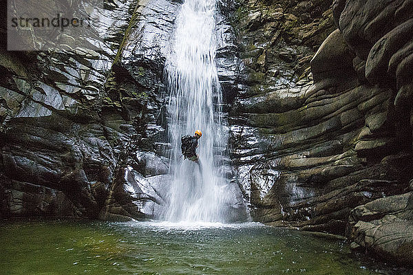 Mann seilt sich über einen Wasserfall ab und nähert sich einem tiefen Becken  Vancouver B.C.
