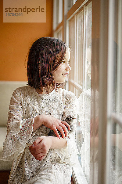 Ein kleines glückliches Mädchen  das sich im Fenster spiegelt  hält ein Küken in den Händen