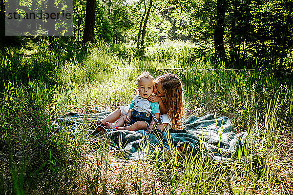 Schwester küsst Kleinkind Bruder draußen im hohen Gras