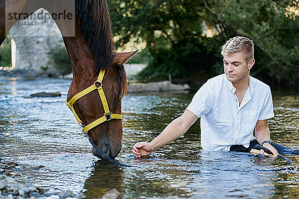 Porträt eines blonden jungen Mannes mit einem Pferd an einem Fluss