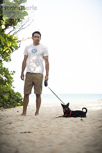 Junger fitter Mann geht mit seinem Hund am Strand von Hawaii spazieren