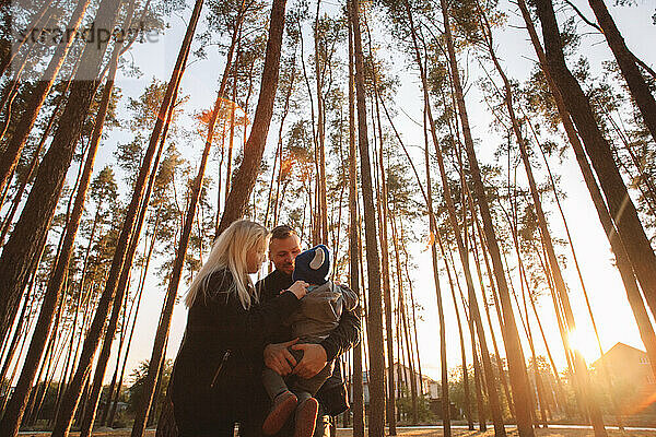 Glückliche junge Familie steht im Wald bei Sonnenuntergang im Herbst