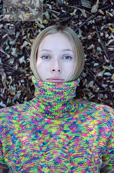 Nahaufnahme einer jungen Frau in einem Pullover  die im Herbstwald liegt.
