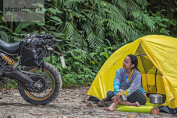 Frau  die sich auf dem Campingplatz entspannt und auf ihr Scrambler-Motorrad schaut
