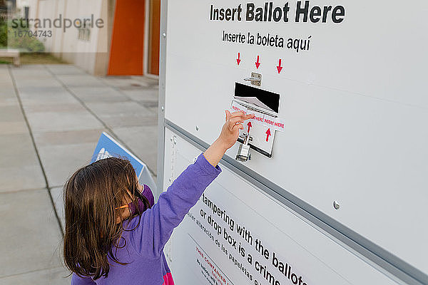 Ein Kind mit Gesichtsmaske wirft seinen Stimmzettel in die Briefwahlurne