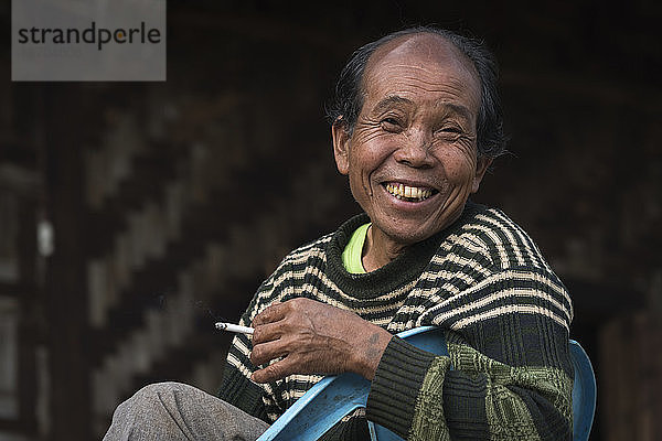 Fröhlicher birmanischer Mann vom Stamm der Palong  der im Freien sitzend eine Zigarette raucht  in der Nähe von Hsipaw  Myanmar
