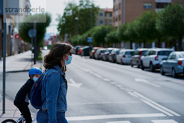 Frau auf der anderen Straßenseite mit einer Maske und Sonnenbrille