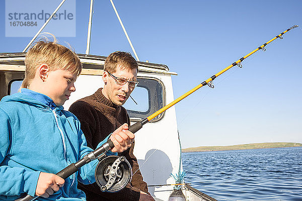 Männlicher Fischer unterrichtet Jungen beim Fischen auf einem Boot