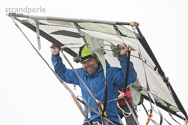 Porträt eines Bergsteigers  der ein Portaledge über dem Kopf trägt.