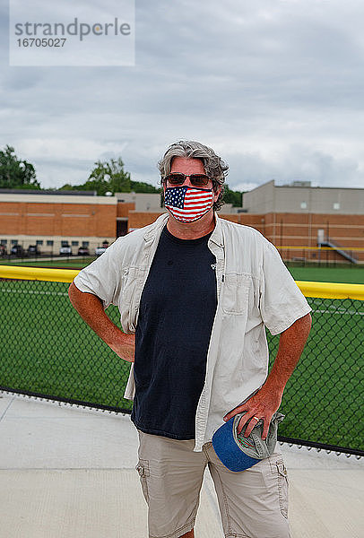 Obere Hälfte eines Mannes mit einer Maske mit amerikanischer Flagge vor einer High School