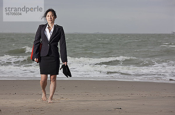 Geschäftsfrau geht am leeren Strand und hält ihre Schuhe