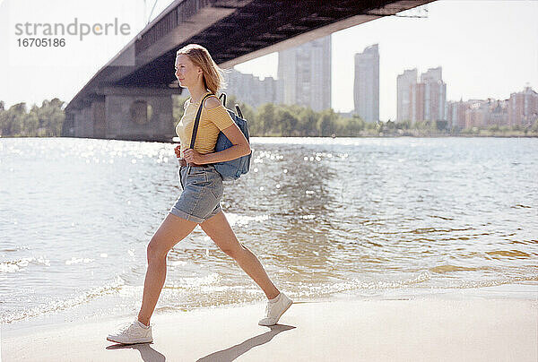 Junge Frau mit Rucksack zu Fuß unter der Brücke in der Nähe des Flusses