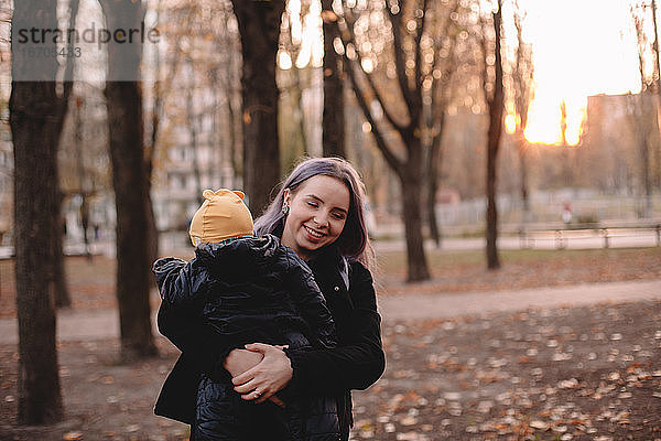 Glückliche junge Mutter mit Baby Sohn im Park im Herbst bei Sonnenuntergang