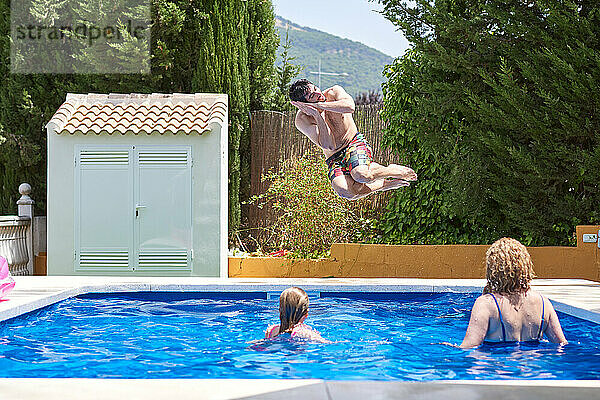 Junger Mann springt in einen Pool. Genießen Sie die Ferien mit Ihrer Familie.