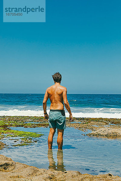 Junger Mann steht im Wasser und schaut von einer Steilküste in Baja auf den Ozean hinaus.
