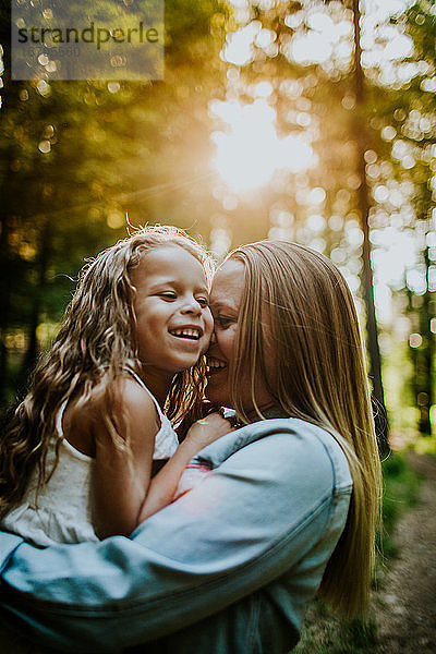 Glückliche Mutter und Tochter lachend und kuschelnd im beleuchteten Wald