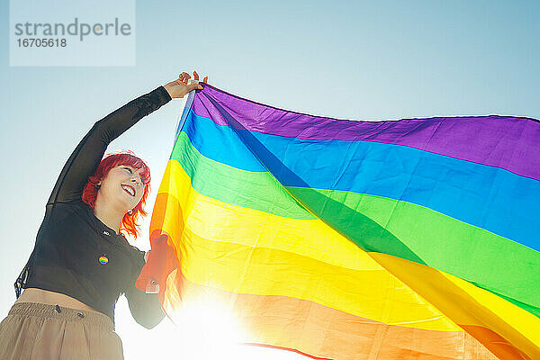 Junges Mädchen hisst LGBT-Flagge auf der Straße bei Tageslicht