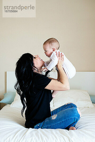 Charmante brünette Frau spielt mit ihrem Baby  während sie auf dem Bett sitzt