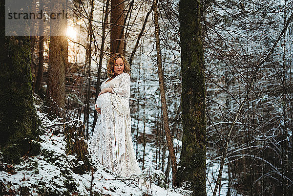 Vorderansicht einer schwangeren Frau im Wald mit der Sonne im Rücken