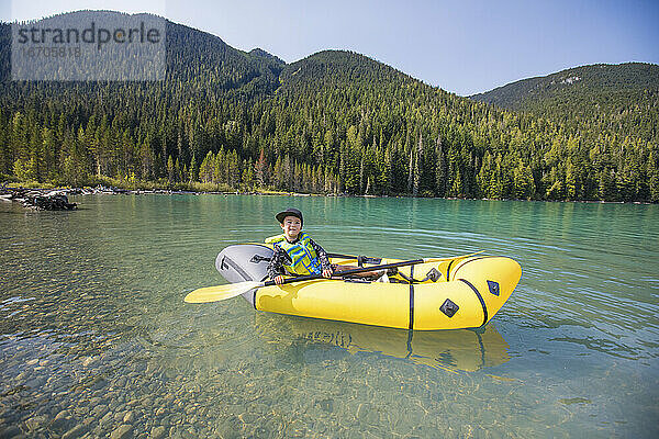 Junge paddelt in einem gelben Packraft-Boot auf einem malerischen See in der Nähe von Whistler.