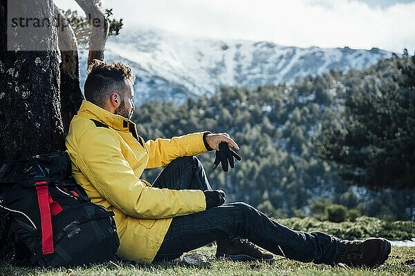 Junger Mann mit gelber Jacke und Rucksack auf dem Berg sitzend.