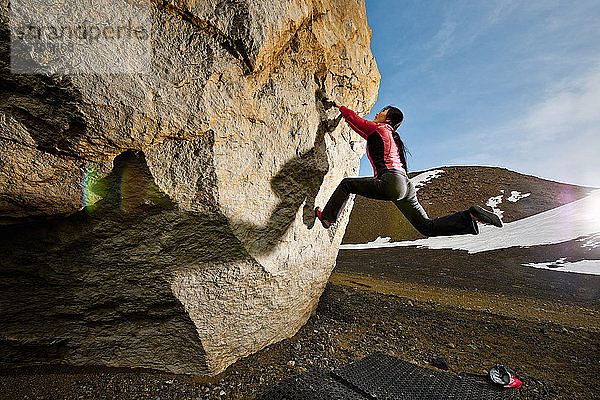 Frau beim Bouldern am Felsen im ländlichen Island