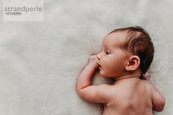 Neugeborenes Baby liegt auf einer weißen Decke und schaut zur Seite