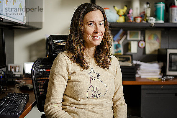 Eine Professorin sitzt an ihrem Bürotisch und lächelt mit direktem Blick