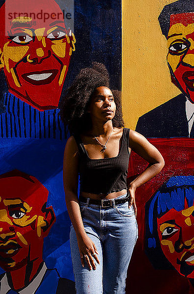 Eine schöne junge Künstlerin in goldenem Licht lehnt sich an ihr Wandgemälde