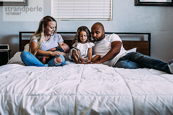 Eine Familie  die mit ihrem neugeborenen Baby auf dem Bett kuschelt