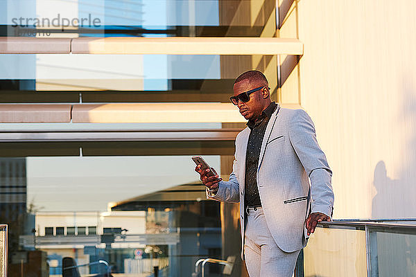 Afroamerikanischer Geschäftsmann mit Mobiltelefon an einem Sommernachmittag.