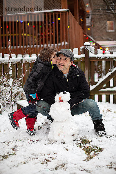 Der Sohn küsst seinen Vater  nachdem sie in ihrem Garten einen Schneemann gebaut haben