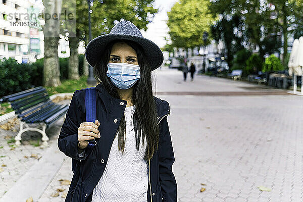 Schönes junges Mädchen mit Hut und Maske in der Stadt stehend