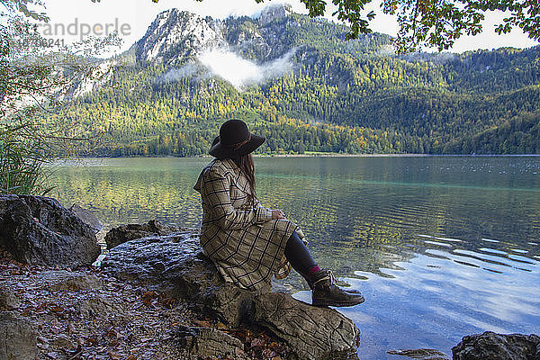 Eine Frau sitzt auf einem Felsen an einem Alpensee in Deutschland