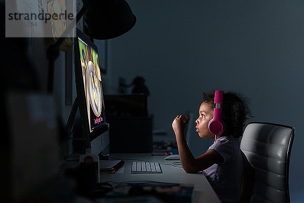Junges Mädchen mit Kopfhörern am Computer zu Hause