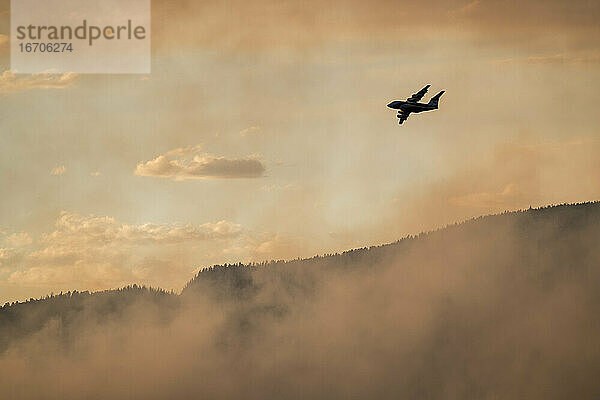 Silhouette Flugzeug fliegen über Rauch aus einem Waldbrand in Wald