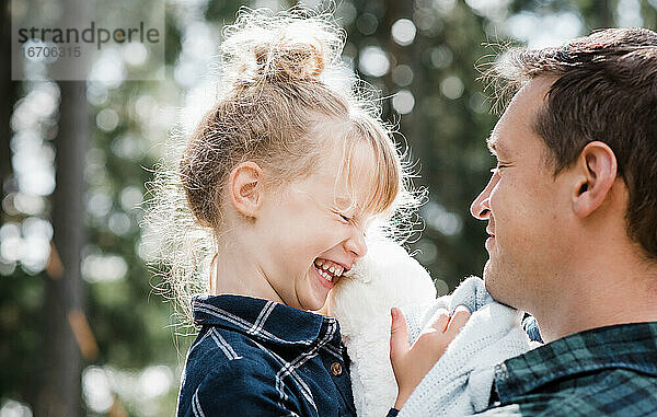 Kleines Mädchen lacht mit ihrem Vater  der sie trägt  und lächelt sie an